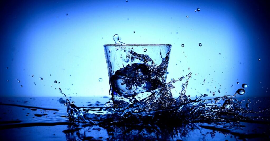 Vibrant close-up of water splashing in a glass, capturing dynamic motion and reflections.