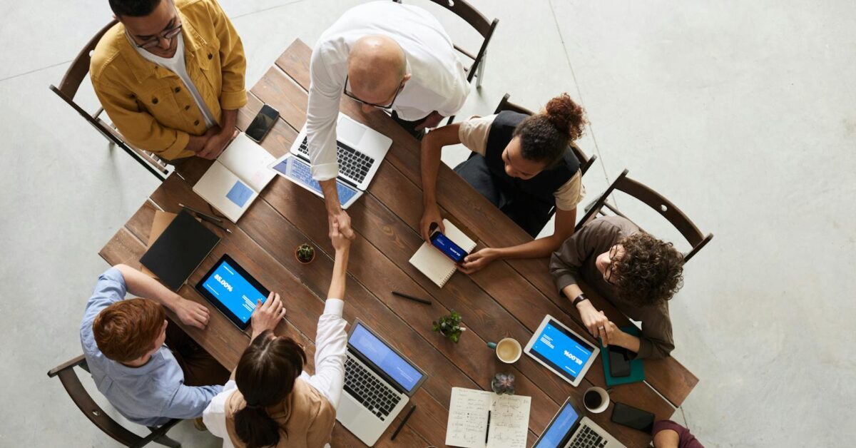 Top view of a diverse team collaborating in an office setting with laptops and tablets, promoting cooperation.