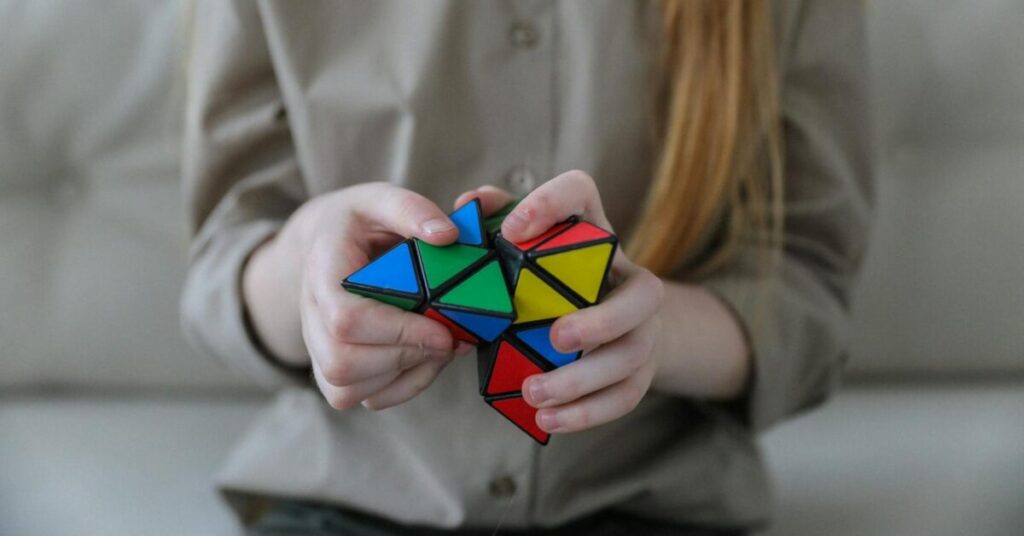 Crop anonymous girl demonstrating and solving colorful puzzle with triangles in soft focus